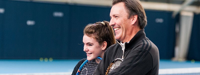 child and adult standing next to each other holding their rackets and smiling 