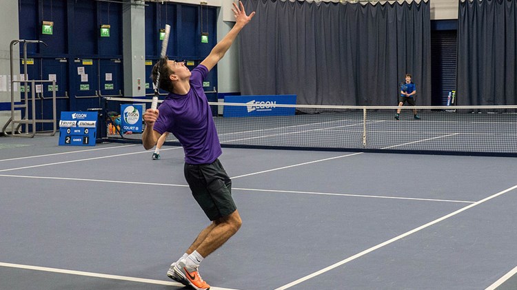 doubles match being played on indoor court with one player serving