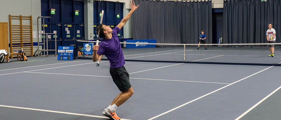 doubles match being played on indoor court with one player serving