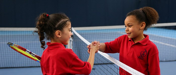two kids wearing red tops shaking hands over net on tennis court