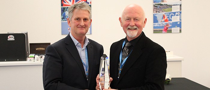 keith reynolds and coty in suits both holding one glass trophy between them