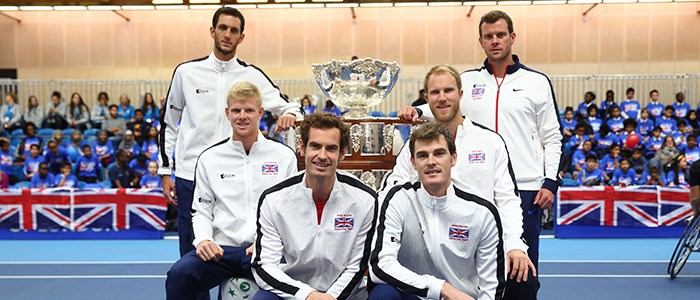 6 members of davis cup team standing and sitting around big silver trophy with GB flags at the bag