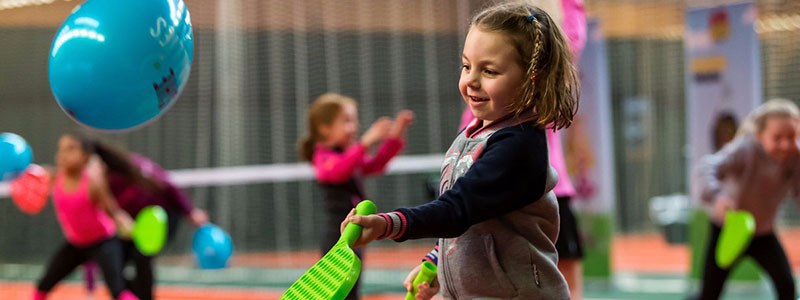 little child playing with plastic green tennis racket hitting blue balloon