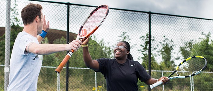 Two people high fiving while playing tennis with courtside fence in background