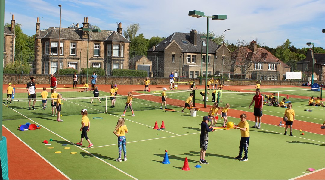 Children playing on a busy tennis court doing sports activities using cones and balls