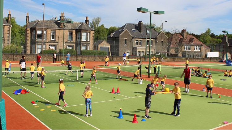 Children playing on a busy tennis court doing sports activities using cones and balls