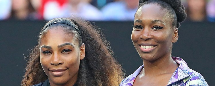 Serena and Venus Williams smiling next to each other on a tennis court