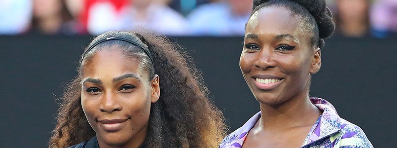 Serena and Venus Williams smiling next to each other on a tennis court