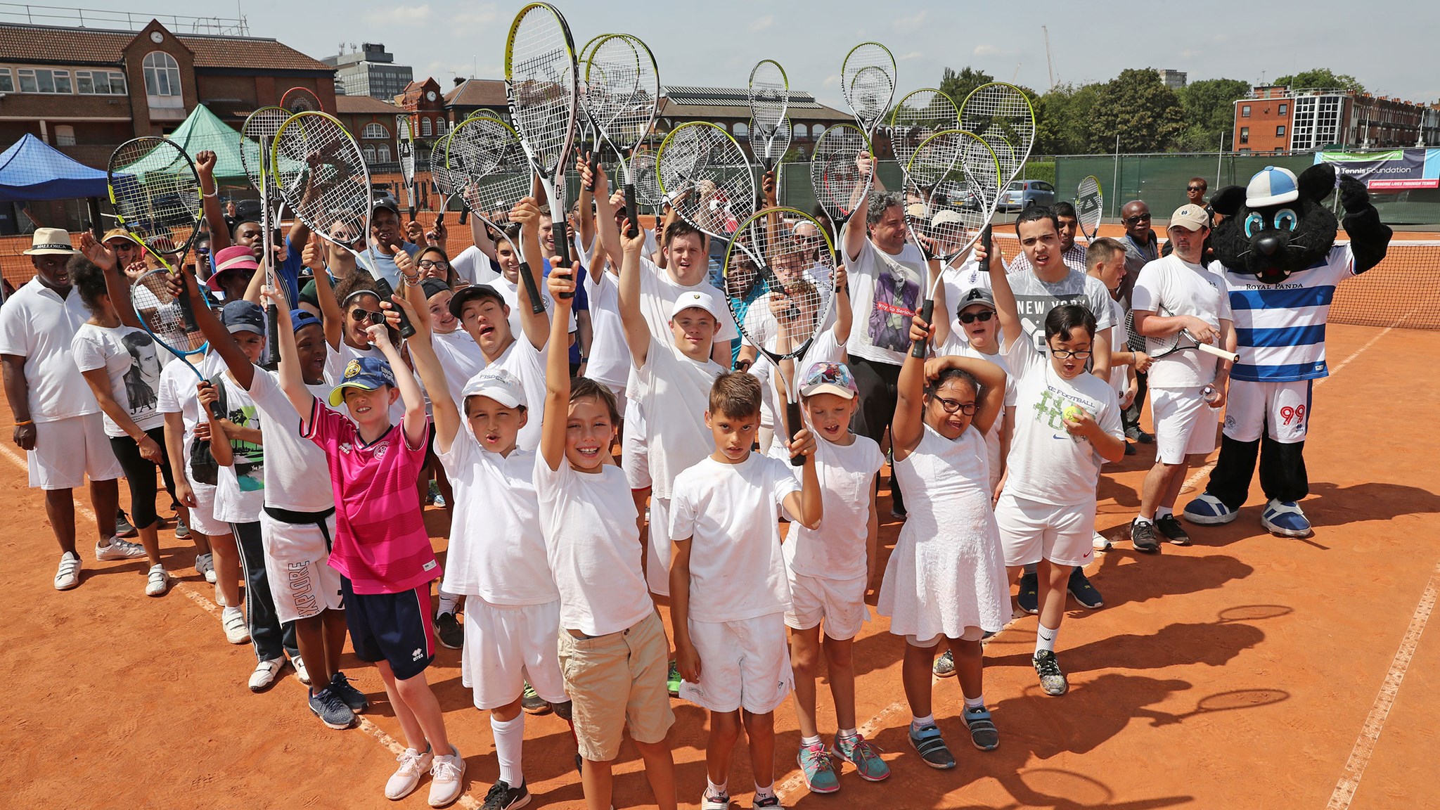 group of young tennis students posing on court holding their rackets up