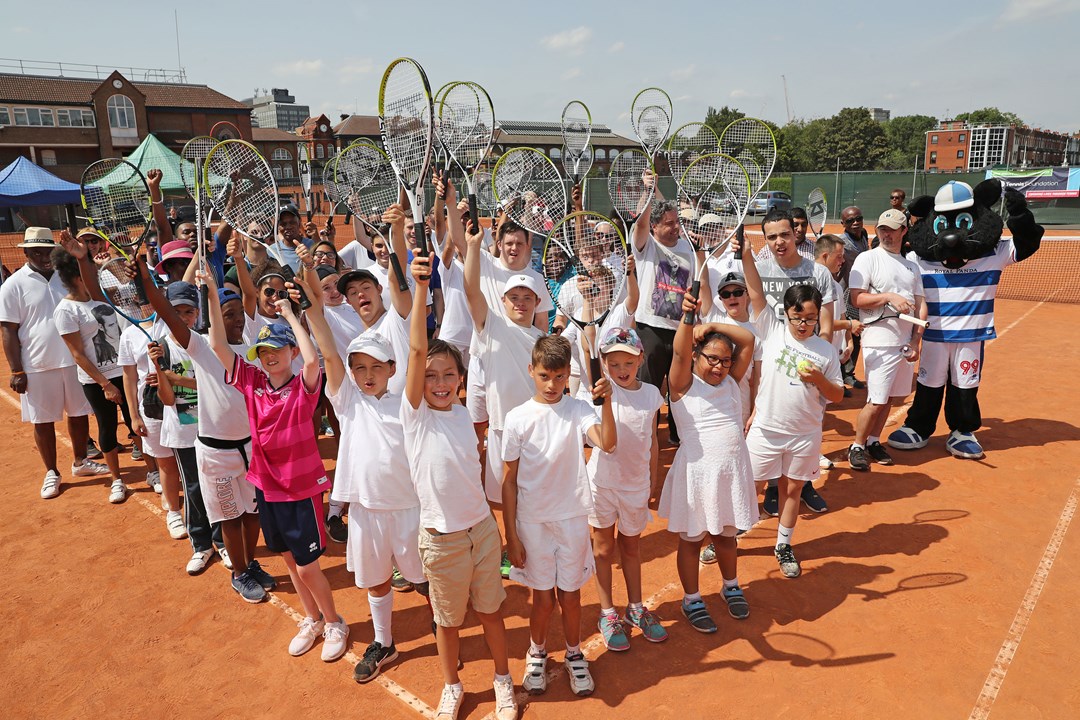 group of young tennis students posing on court holding their rackets up
