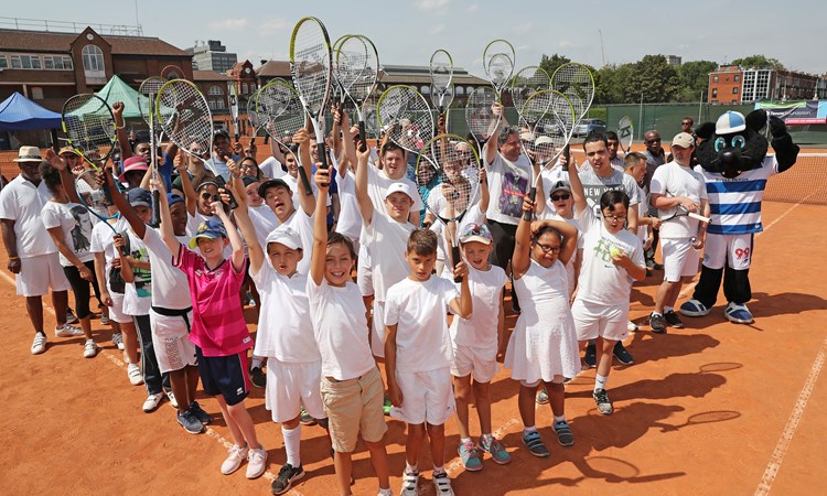 group of young tennis students posing on court holding their rackets up