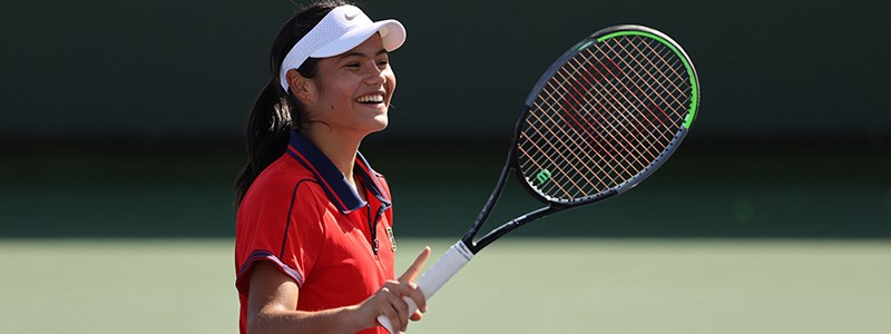 Emma Raducanu smiling with her tennis racket and white nike tennis cap on