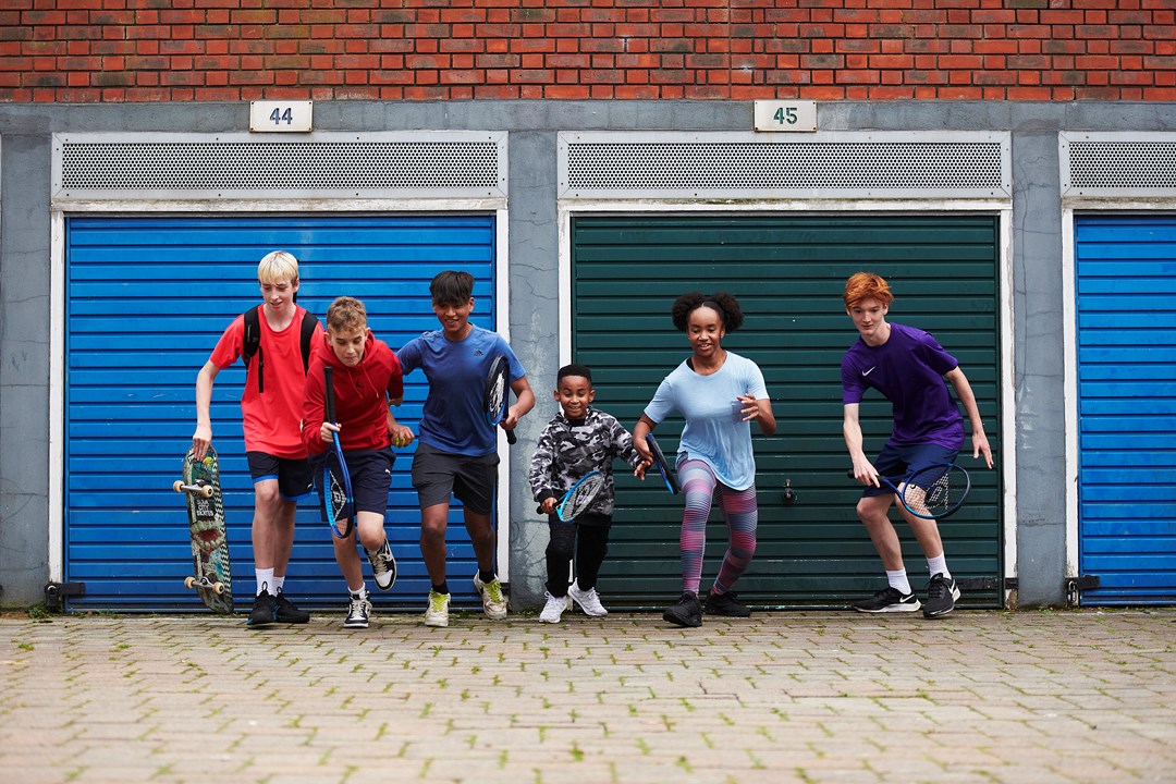 Kids holding tennis rackets running with colourful garage doors in background