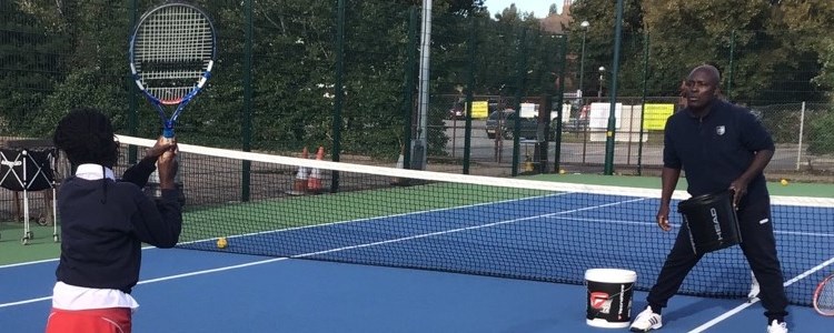 Isaac Frimpong coaching a young child tennis on an outdoor tennis court