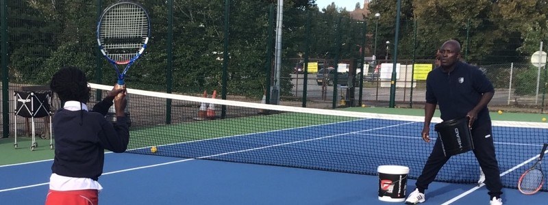 Isaac Frimpong coaching a young child tennis on an outdoor tennis court