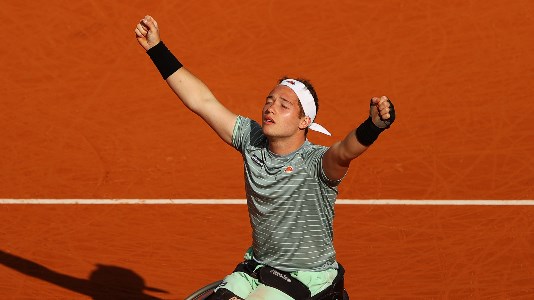 Alfie Hewett rejoicing with his arms raised on a clay tennis court