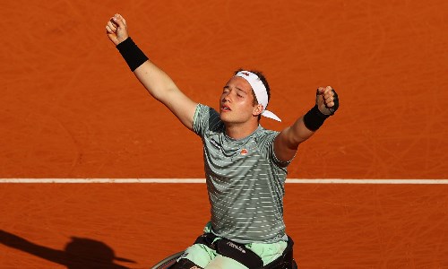 Alfie Hewett rejoicing with his arms raised on a clay tennis court