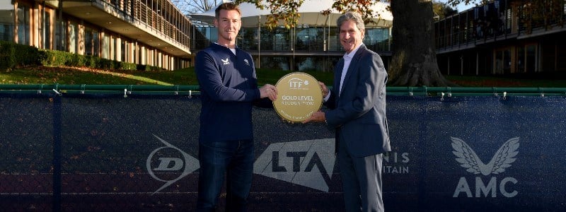 two men hlding gold standard ITF trophy between them outside the LTA building