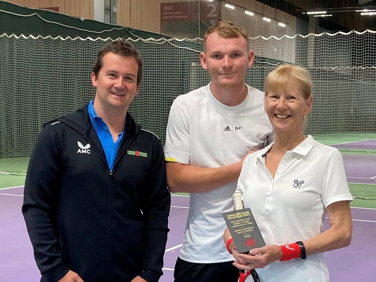 Three people smiling for a picture in an indoor tennis court