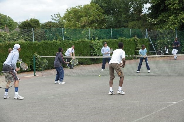 Large tennis game taking place during a tennis lesson