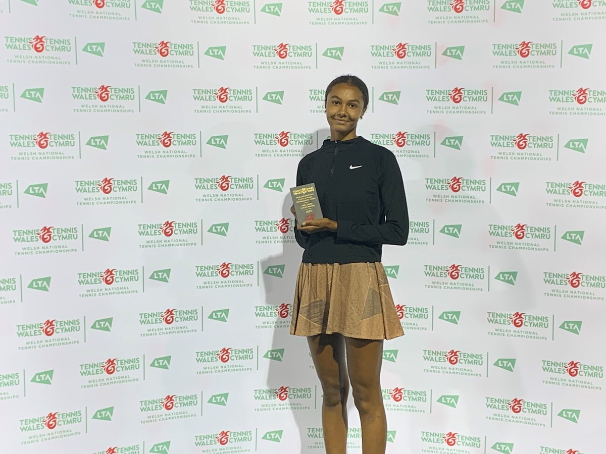 Alex holding her trophy infront of the tennis Wales backdrop