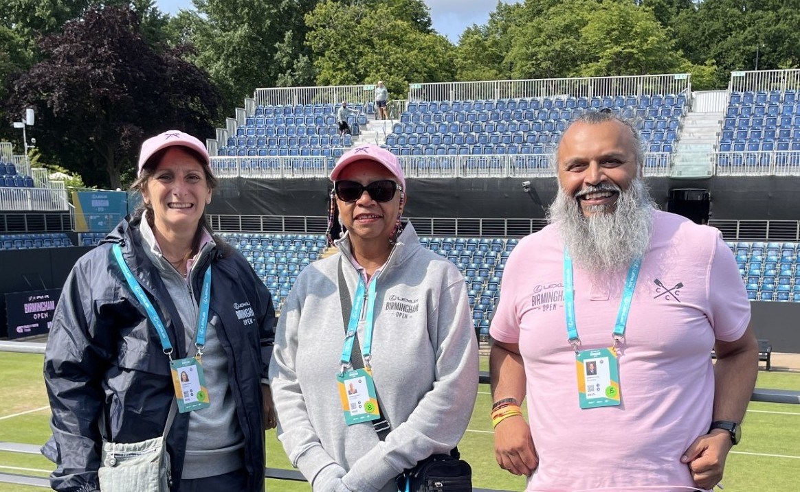 Three volunteers smiling in front of the grass court at the Lexus Birmingham Open