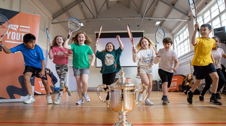 Kids running to a trophy with tennis rackets in hand