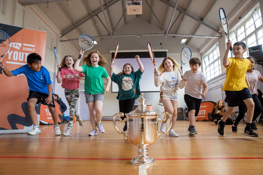 Kids running to a trophy with tennis rackets in hand