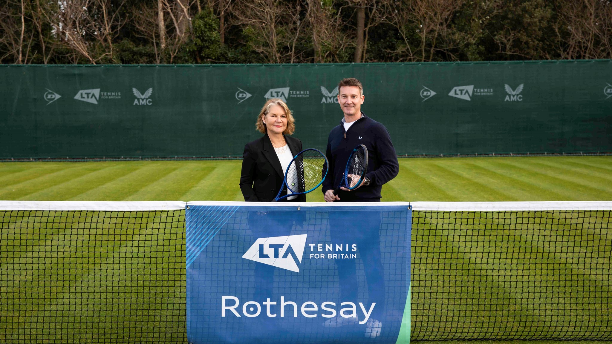 A male and female holding rackets and standing behind a tennis net