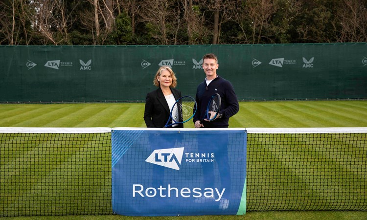 A male and female holding rackets and standing behind a tennis net