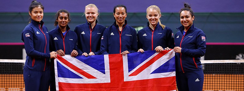 GB fed cup team players standing in front of the net holding large GB flag at the front