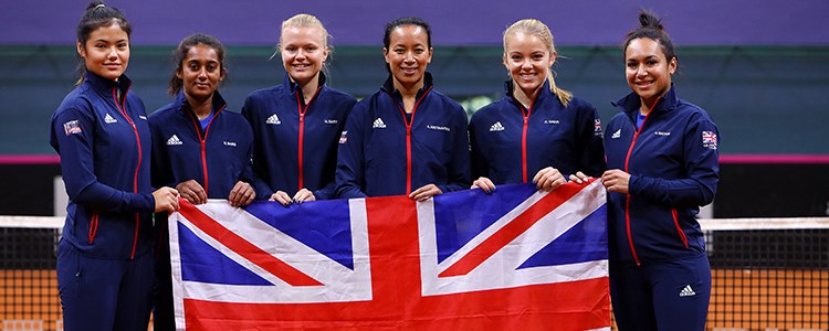 GB fed cup team players standing in front of the net holding large GB flag at the front