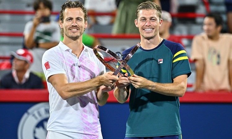 Two male tennis players holding one trophy