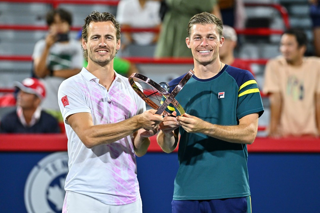 Two male tennis players holding one trophy