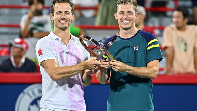 Two male tennis players holding one trophy
