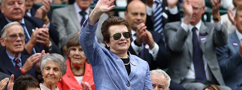 Billie Jean King standing up in a crowd waving and smiling