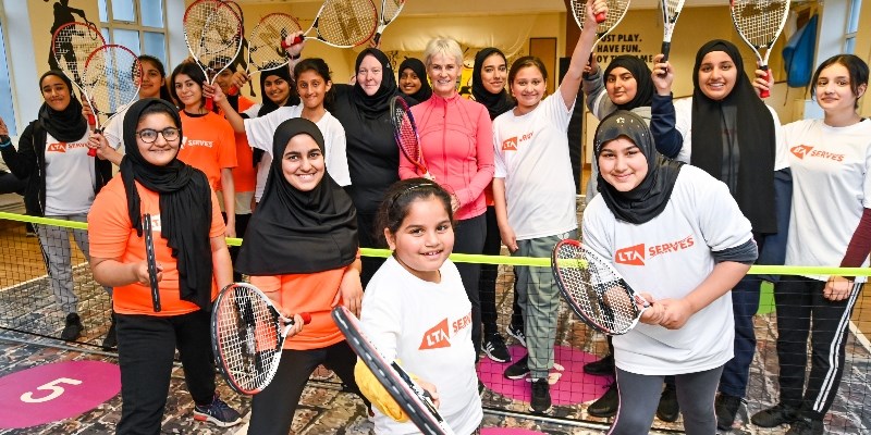 nalette tucker and judy murray standing between a group of kids wearing lta serves tops all holding rackets up 