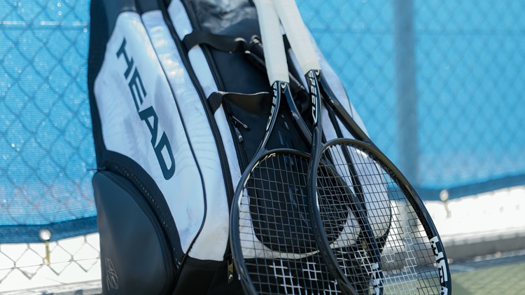 Two tennis rackets leaning against a tennis bag against the court fence. 