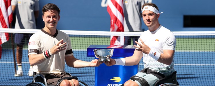 hewett and reid holding trophy in one hand and  other hand holding up four fingers  with us open logo at the back