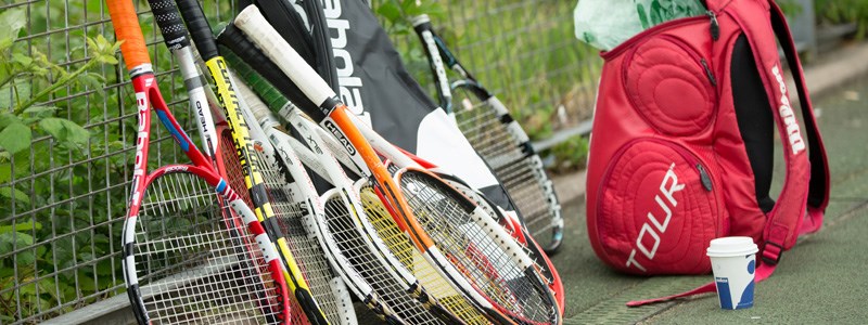 Tennis rackets leaning on fence with wilson red bag besides rackets