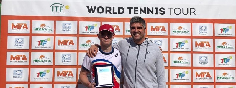 jack pinnington jones standing  besides adult holding trophy with  itf world tennis tour board at the back