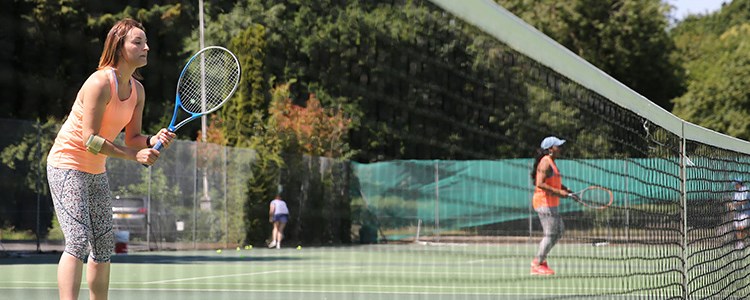 Four adults playing tennis with one getting ready to volley by the net