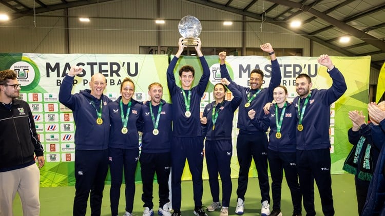A group of men and women smile and raise their hands in the air in celebration. In the middle of the group, a man holds aloft a glass trophy. 