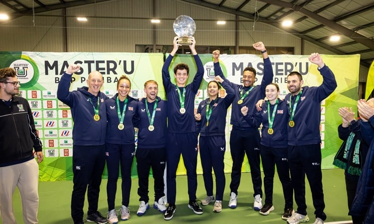 A group of men and women smile and raise their hands in the air in celebration. In the middle of the group, a man holds aloft a glass trophy. 