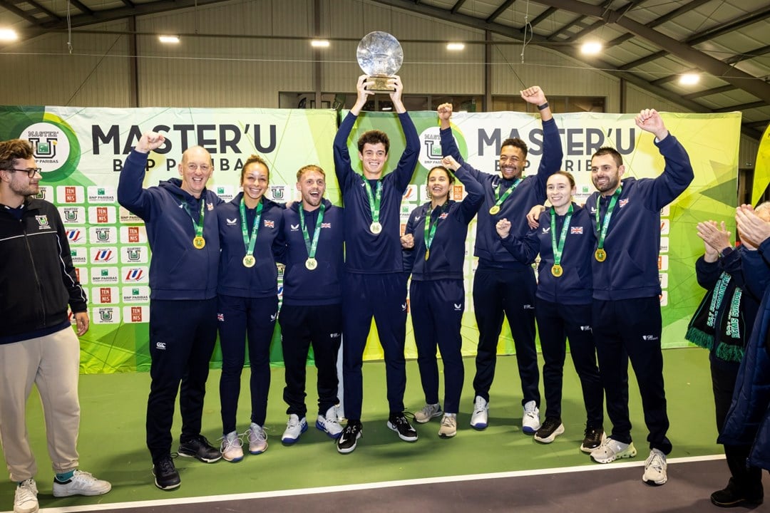 A group of men and women smile and raise their hands in the air in celebration. In the middle of the group, a man holds aloft a glass trophy. 