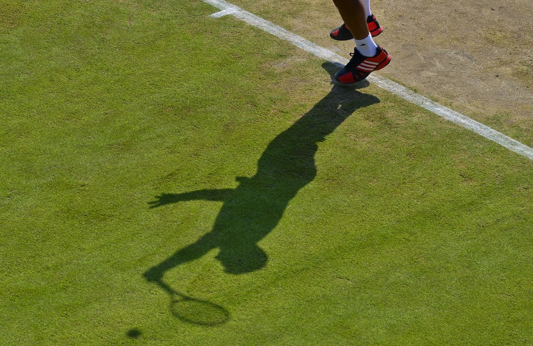 Shadow of player making a serve on grass court