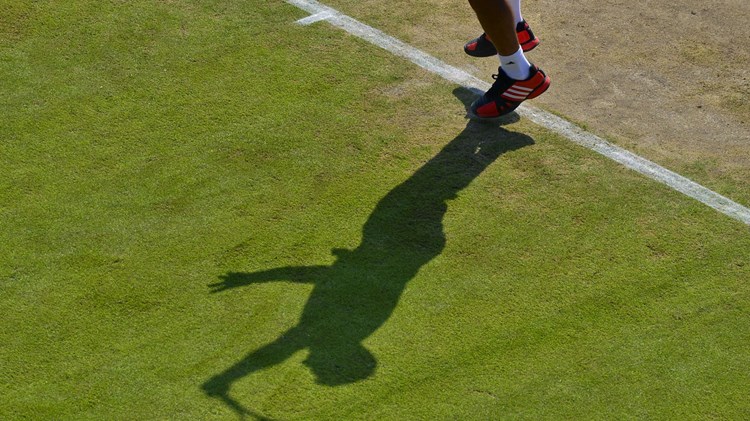 Shadow of player making a serve on grass court
