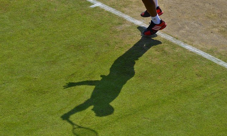 Shadow of player making a serve on grass court