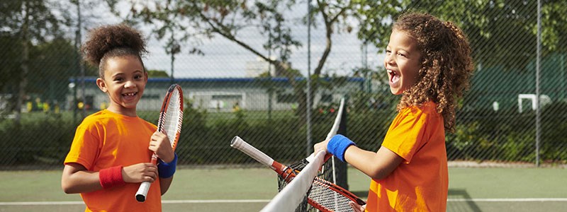 Two junior tennis players smiling and holding rackets