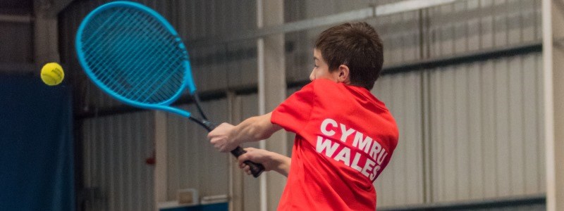 Aiden Coopman returning a shot in an indoors tennis match